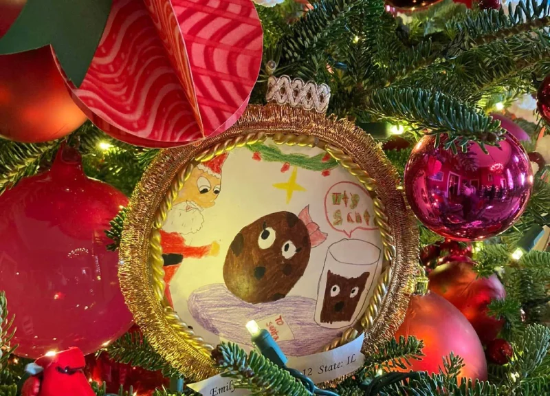 صورة مقرّبة لزينة شجرة عيد الميلاد تظهر رسم طفل محاط بإطار ذهبي. يصور الرسم الملون كعكاً متحركاً وحليباً.