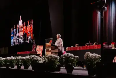 متحدث على المنصة يخاطب حفل التخرج. شاشة كبيرة تعرض نفس المشهد.