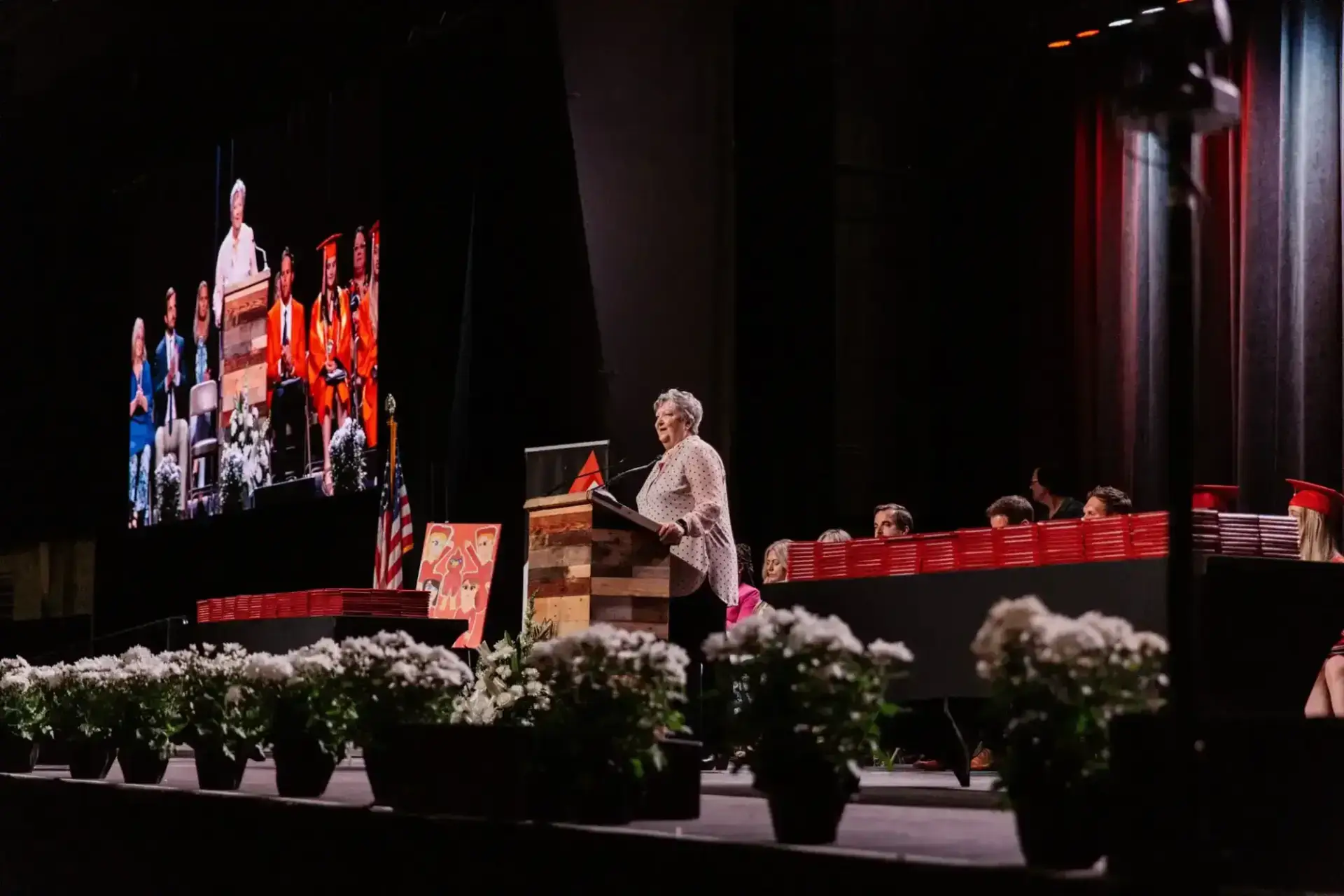 متحدث على المنصة يخاطب حفل التخرج. شاشة كبيرة تعرض نفس المشهد.