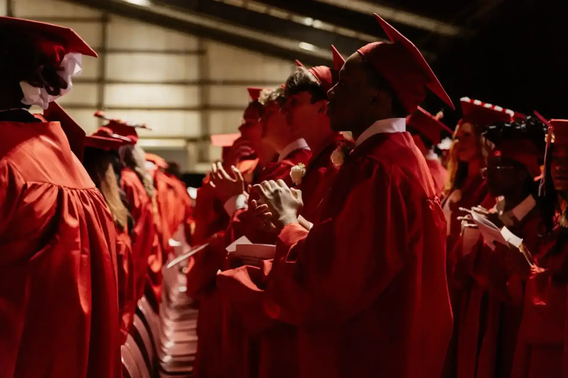 يقف الخريجون الذين يرتدون القبعات والعباءات الحمراء في صفوف متراصة، متجهين إلى الأمام.