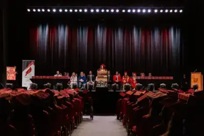 حفل التخرج حيث يجلس الطلاب مرتدين القبعات والعباءات الحمراء في مواجهة المنصة. متحدث على المنصة يحيط به أعضاء هيئة التدريس.