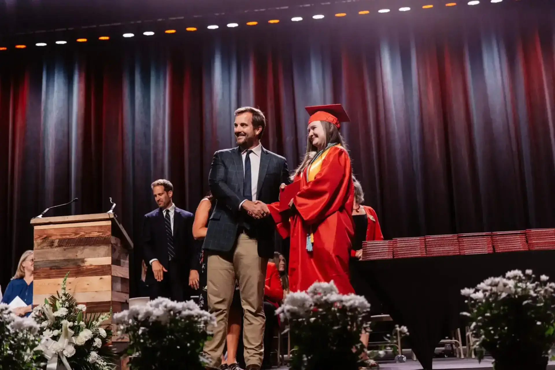 خريج يرتدي ثوباً أحمر يصافح رجلاً مبتسماً في حفل التخرج.