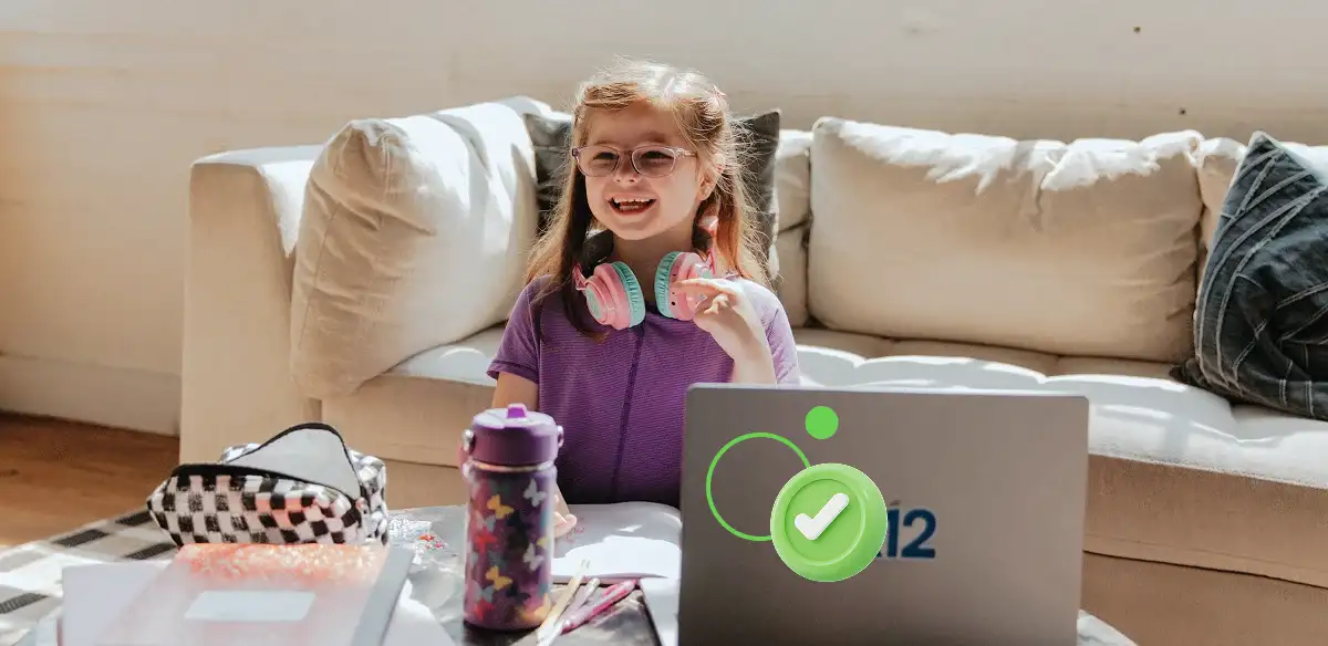 طالبة في المرحلة الابتدائية تعمل على جهاز الكمبيوتر المحمول الخاص بها في المنزل وهي ترتدي سماعات رأس وردية اللون